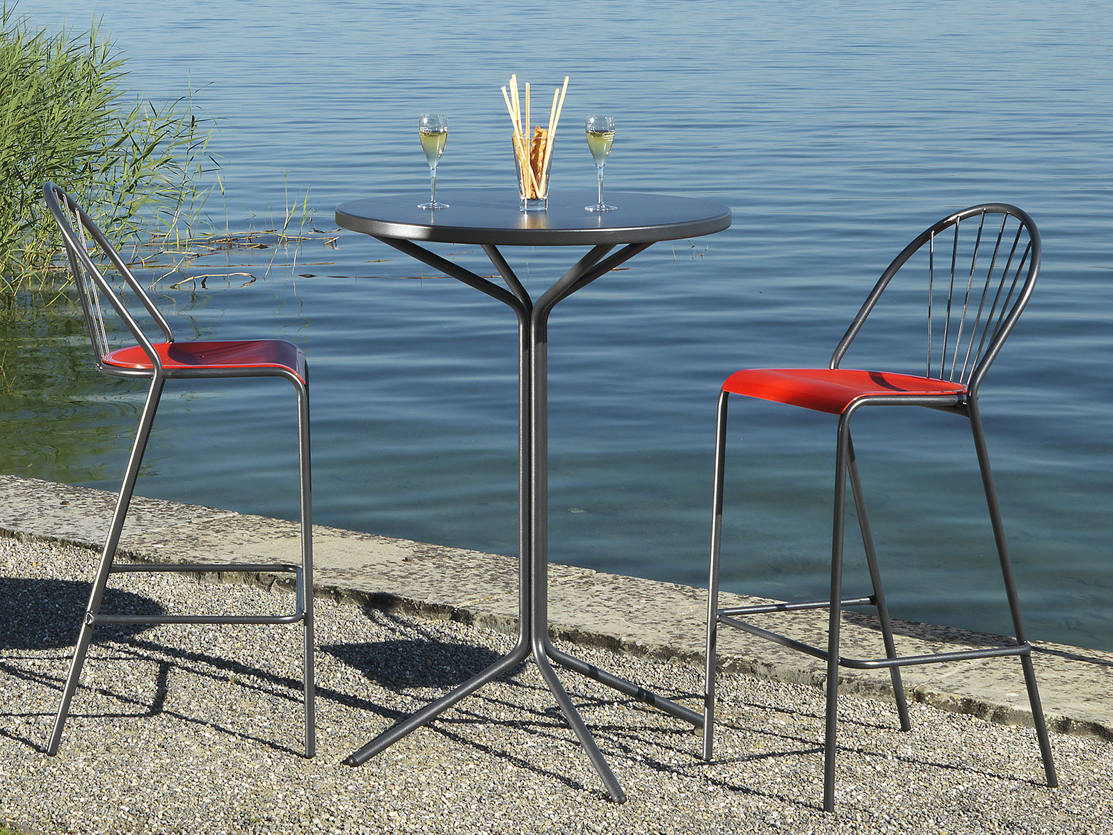 PIX Tisch 110 cm x 60 cm Stehtisch mit zwei Hochstühlen auf einemSteinstrand vor einem See