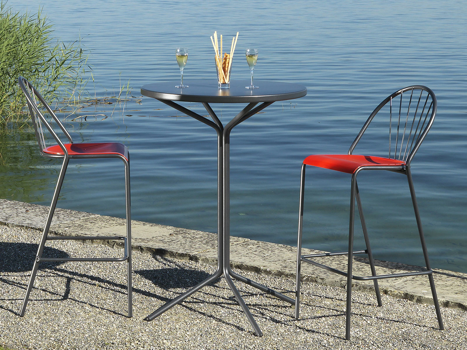 PIX Tisch 110 cm x 60 cm Stehtisch mit zwei Hochstühlen auf einemSteinstrand vor einem See